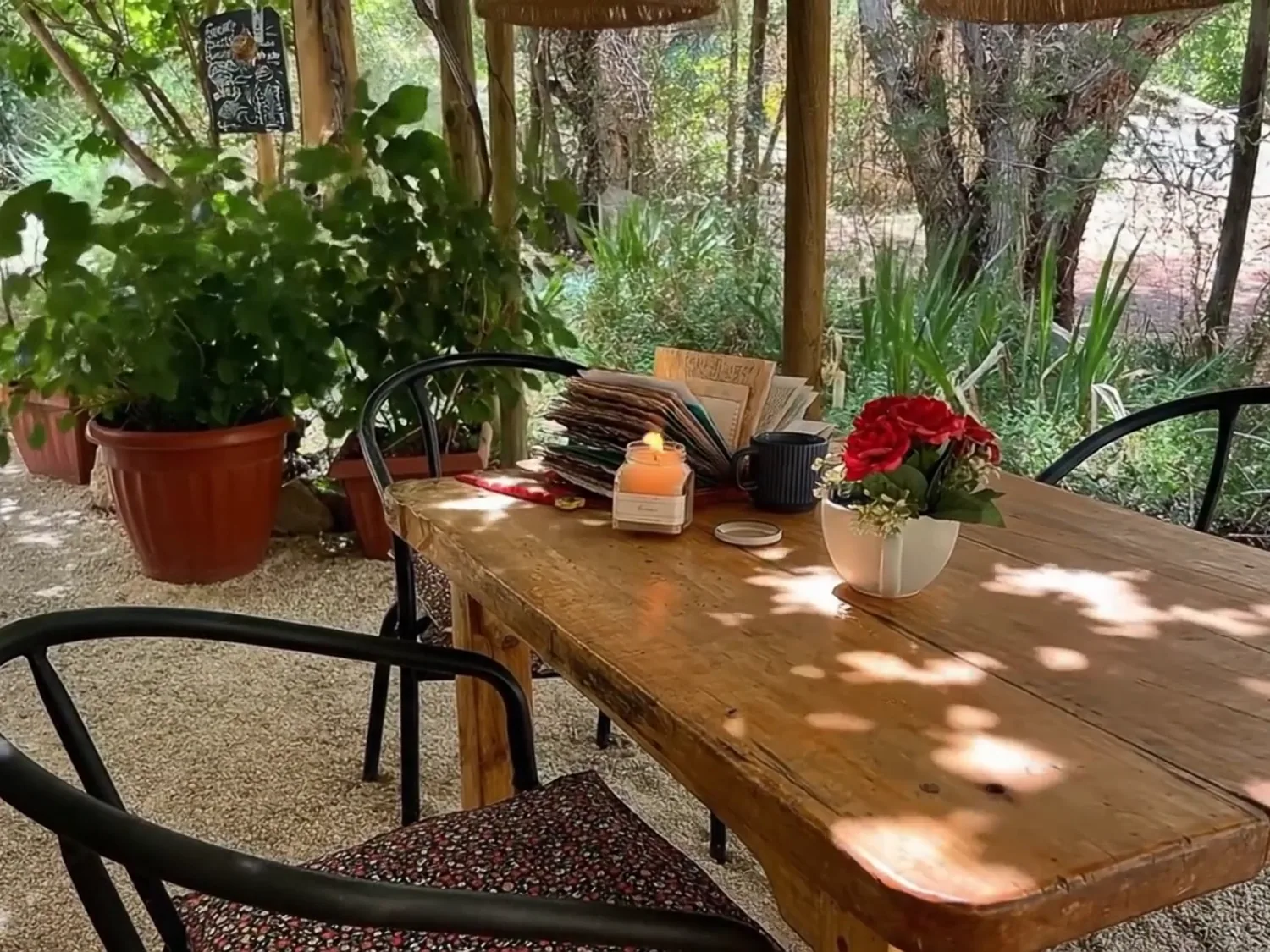 Una mesa de madera puesta bajo la parra, con flores y una vela