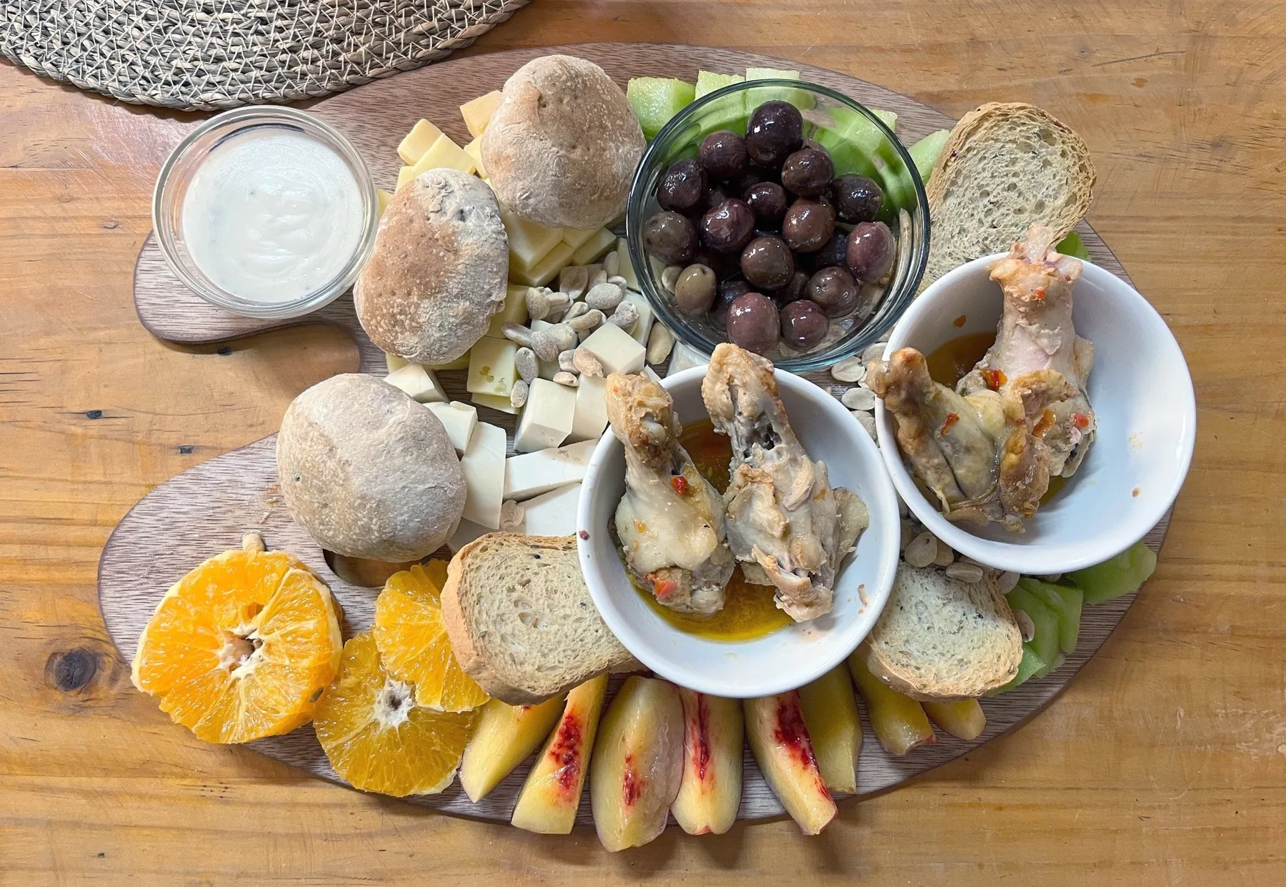 Tabla para compartir: quesos, aceitunas, pan amasado, pollo, naranja y duraznos sobre una tabla de madera