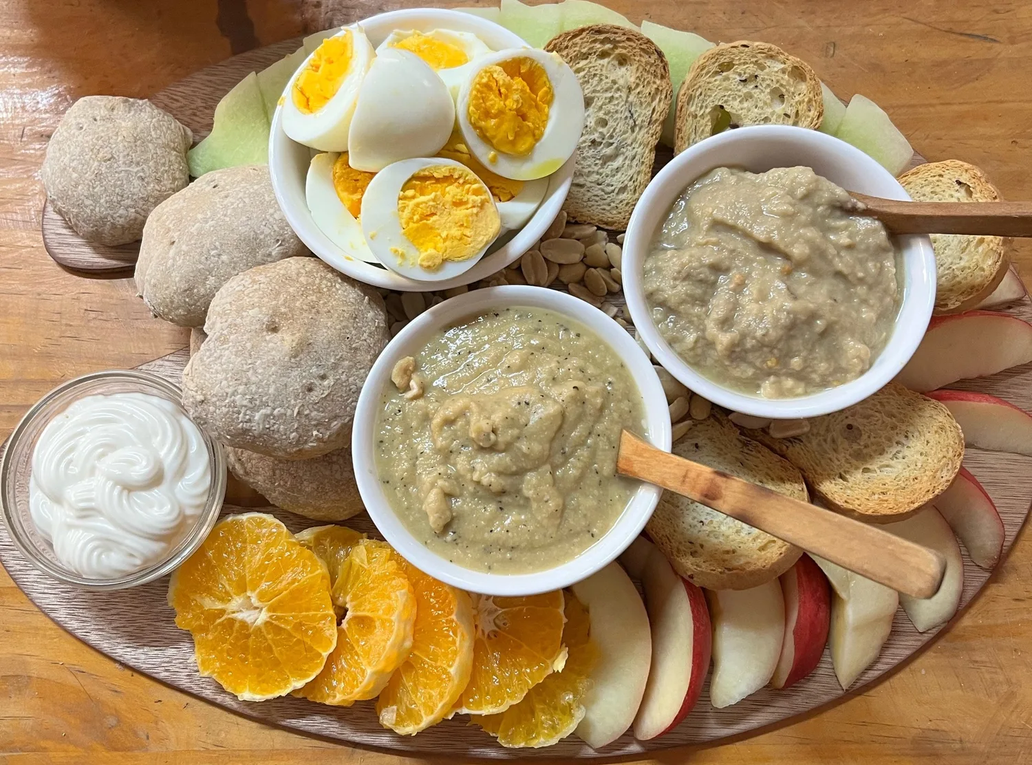 Tabla con huevos duros, dos untables, pan amasado, naranja y manzana